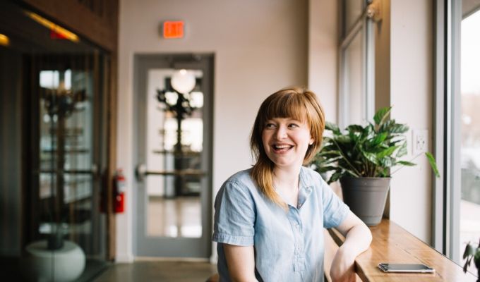 Uśmiechnięta kobieta siedząca przy oknie spoglądająca w bok